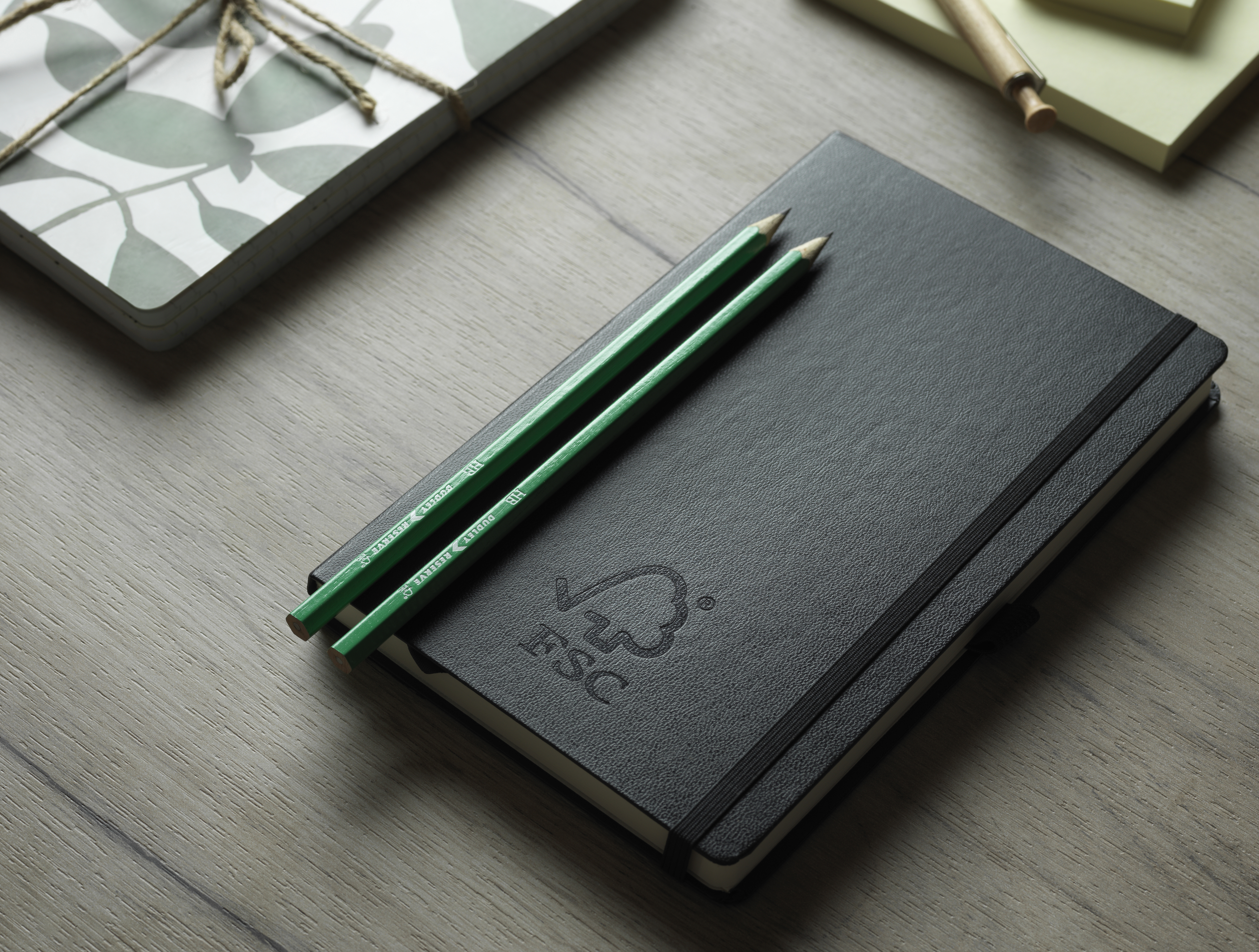 Two Green FSC Certified Pencils Atop Black Notebook with FSC logo 